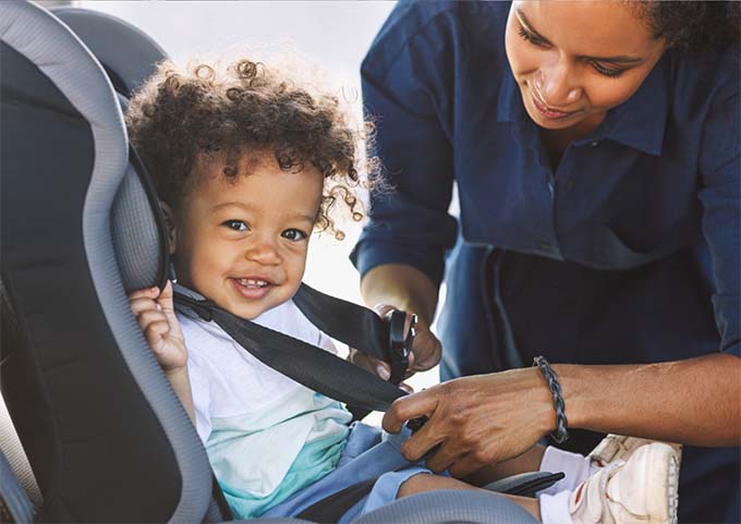 A child being buckled into a car seat by a woman