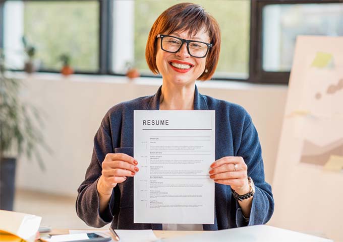 A woman at a desk holding up a resume